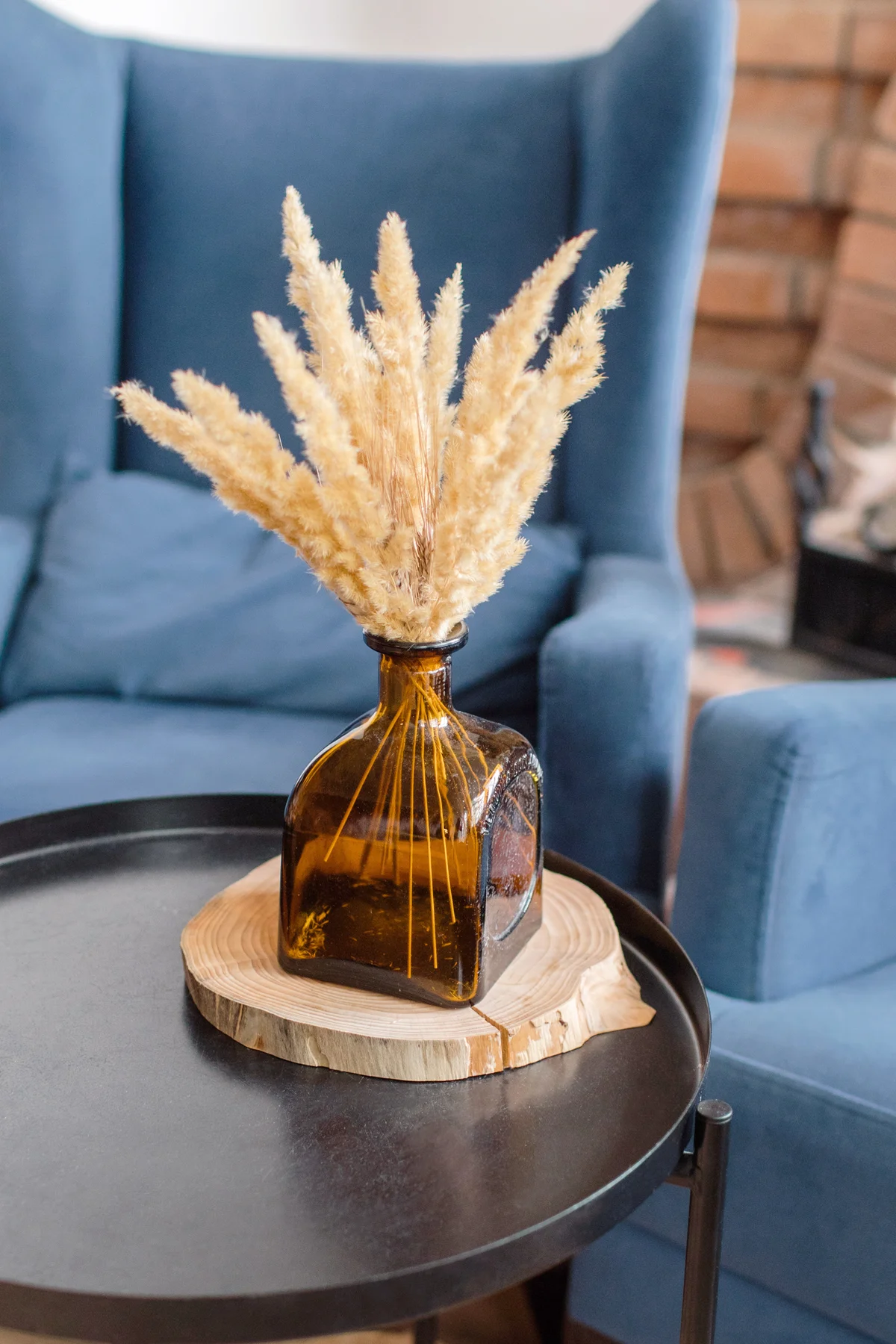 Brown vase with ears of dried flowers on a black metal table against the background of a blue armchair