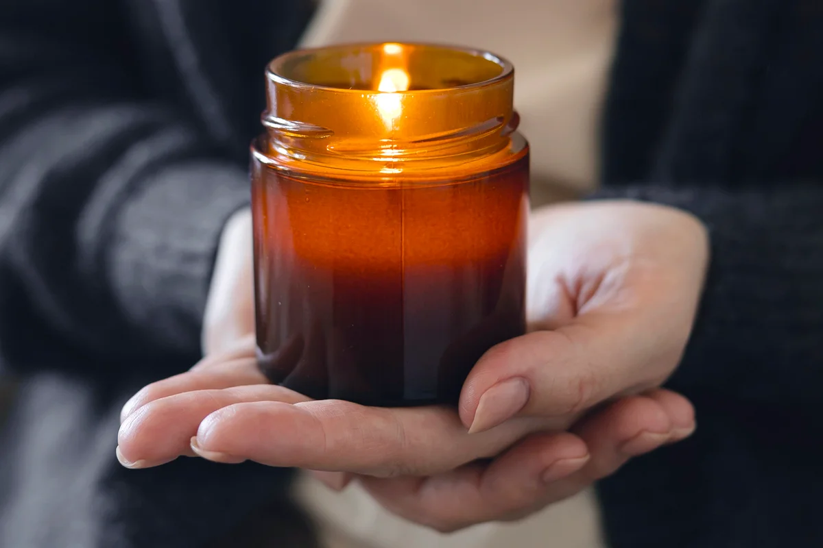 Woman holding in hand burning candle in small amber glass jar