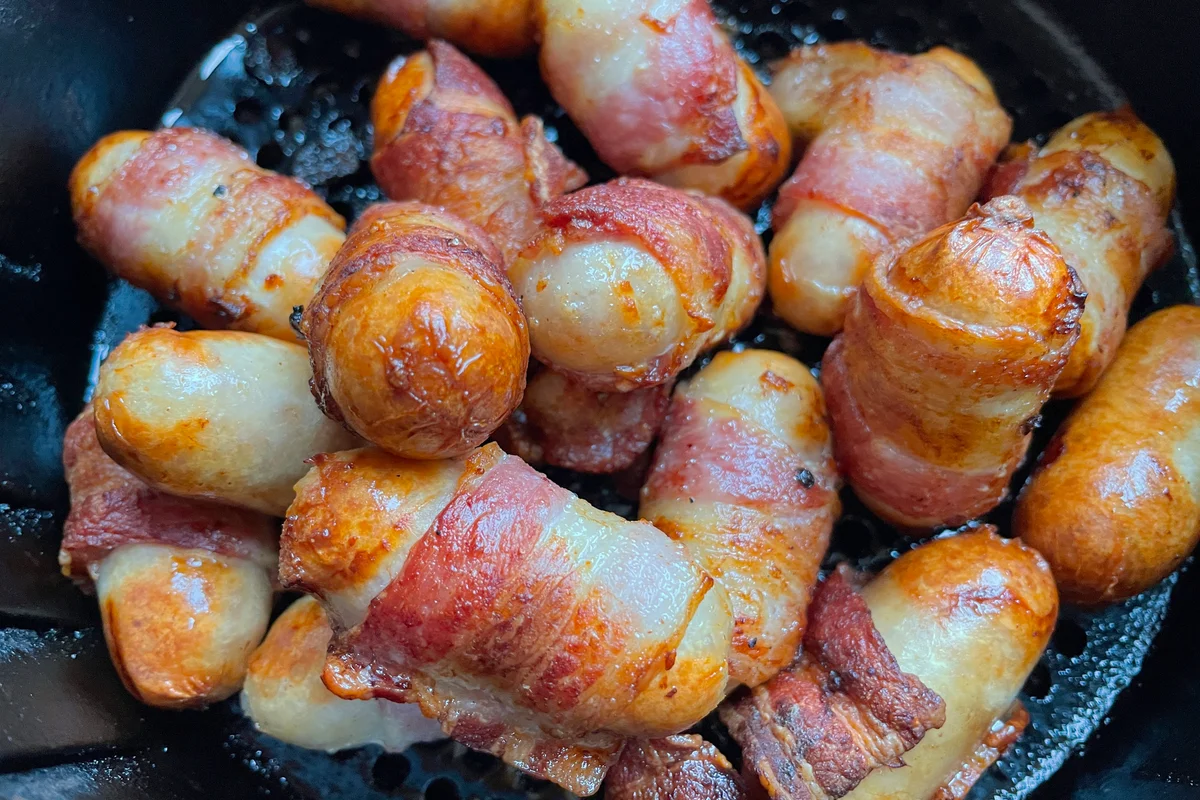Cocktail sausages wrapped in bacon cooking in an air fryer