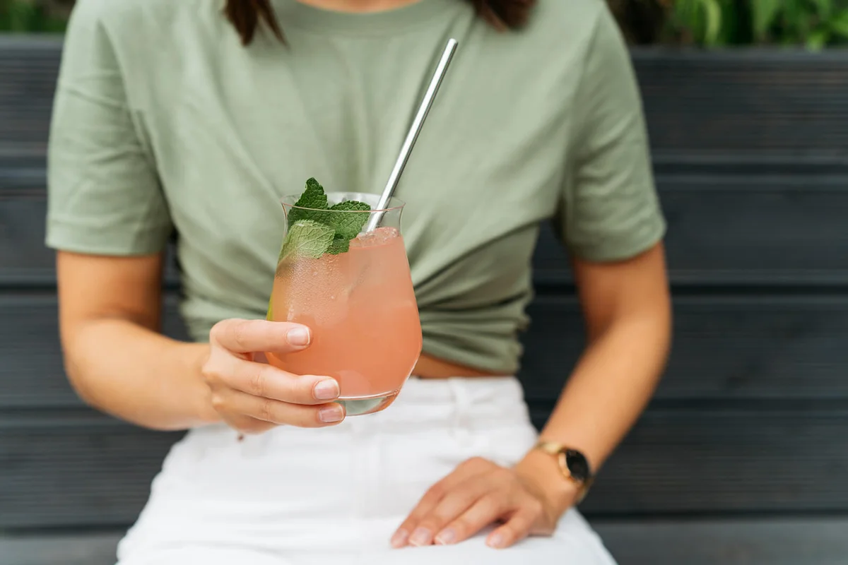 Portrait of a woman with holding a paloma cocktail sitting on a bench