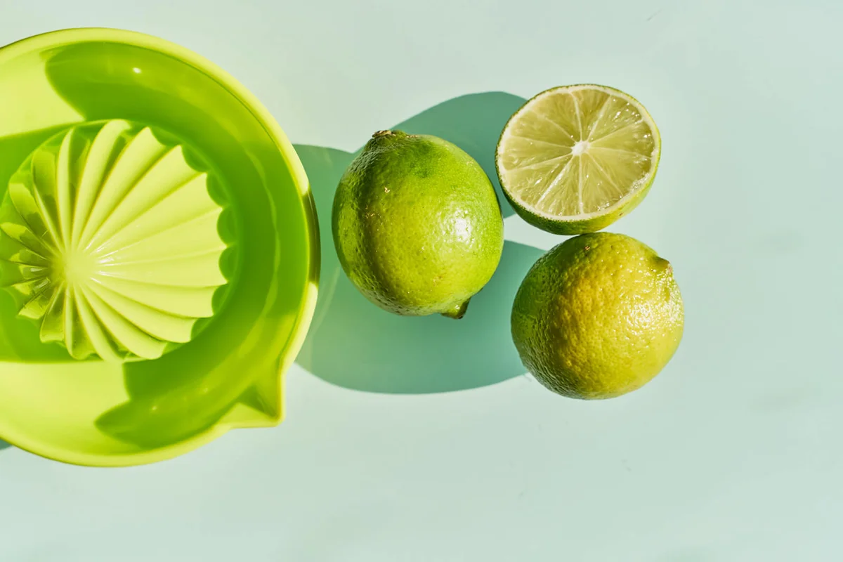 Above view of some green citric limes and a juicer to squeeze them with reflection on the glass mirror of a table