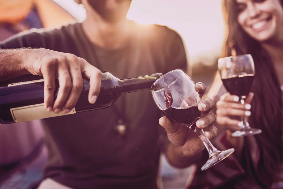 Couple drinking wine outdoors while man is pouring it into a glass