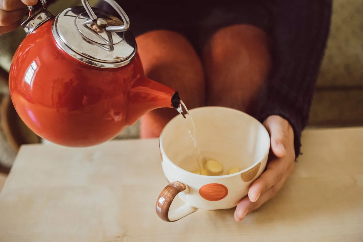 Woman pouring water into tea cup with chopped fresh ginger