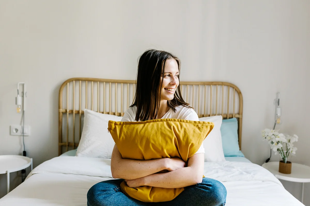Smiling woman embracing pillow on bed at home