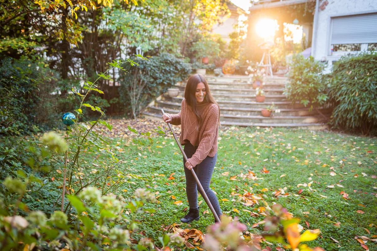 Happy woman sweeping garden with broom in back yard