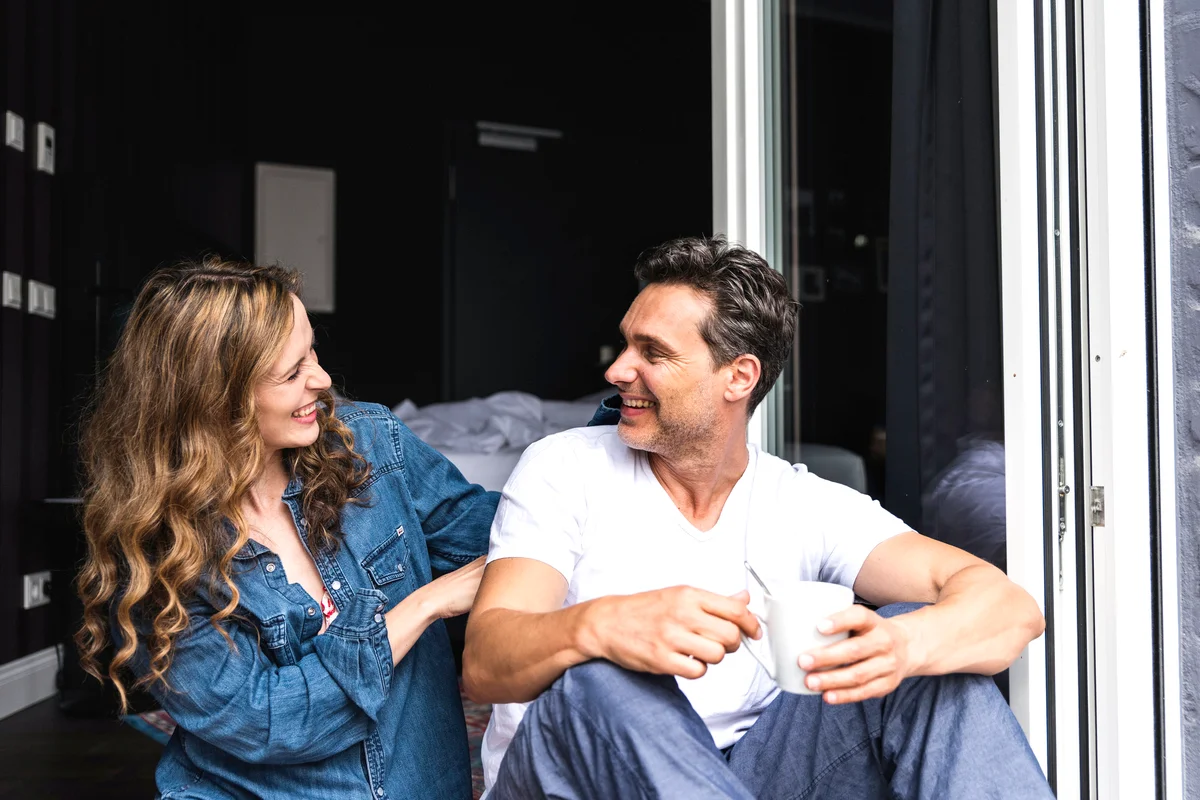 Happy couple in nightwear at home sitting at French window