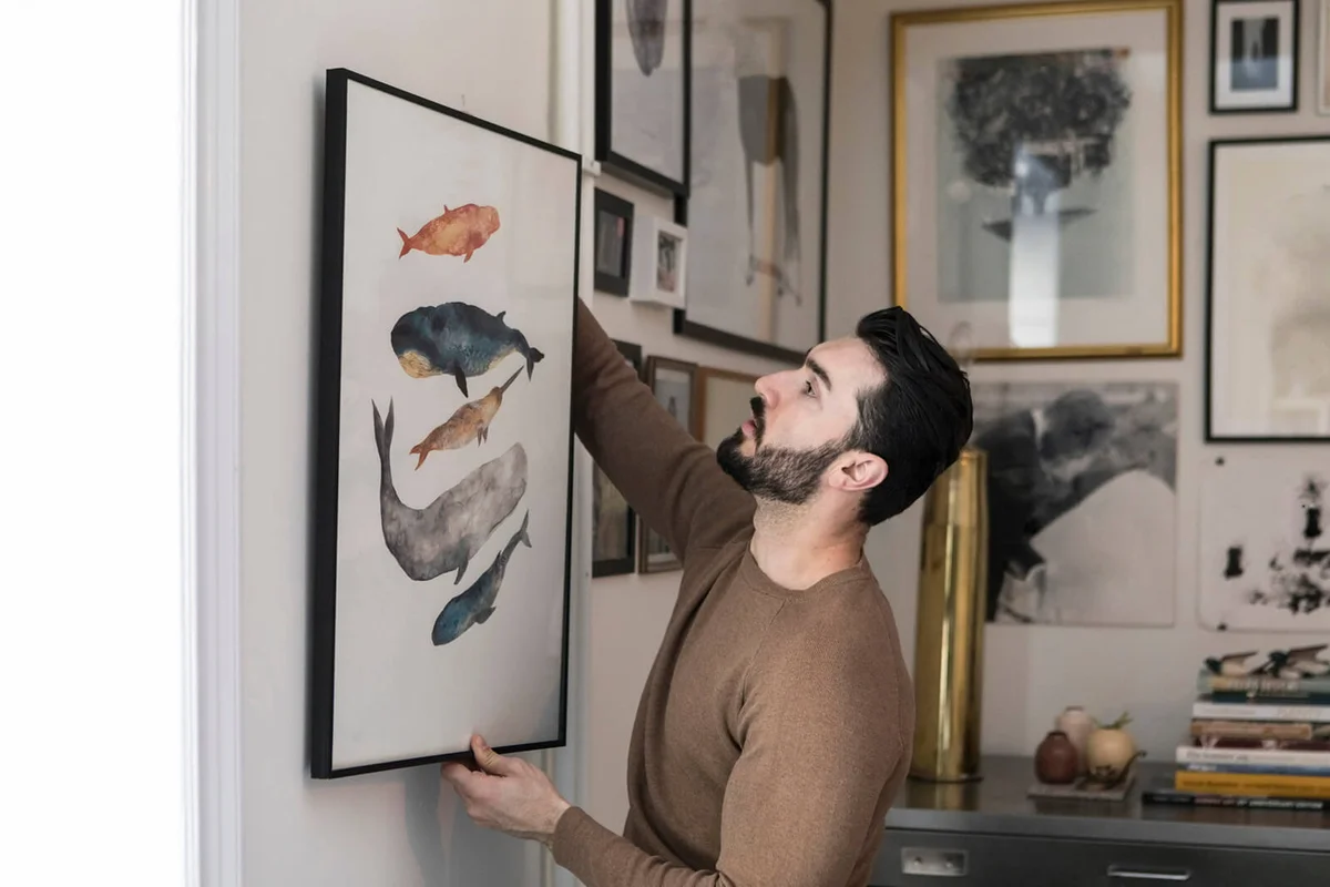 Young man hanging painting on wall at home