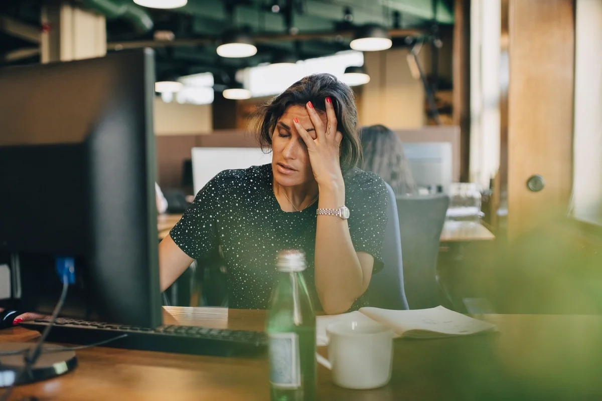 Tired businesswoman with head in hand sitting at computer desk in office