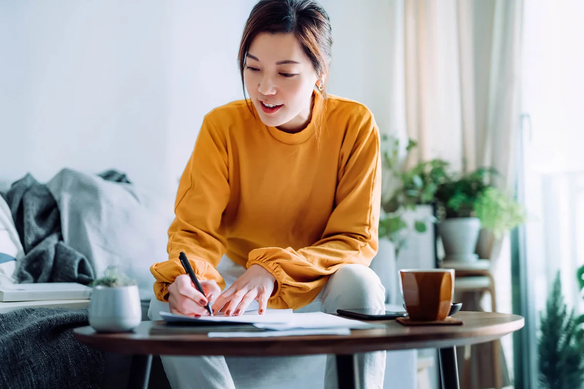 woman holding a pen and signing paperwork in the living room at home