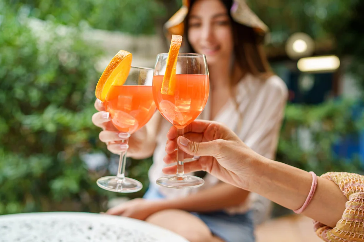 Women in terrace clinking with orange fruit cocktails