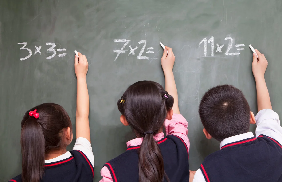 Three school children doing math equations on the blackboard