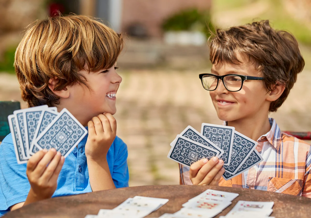 Smiling brothers playing cards at table in yard