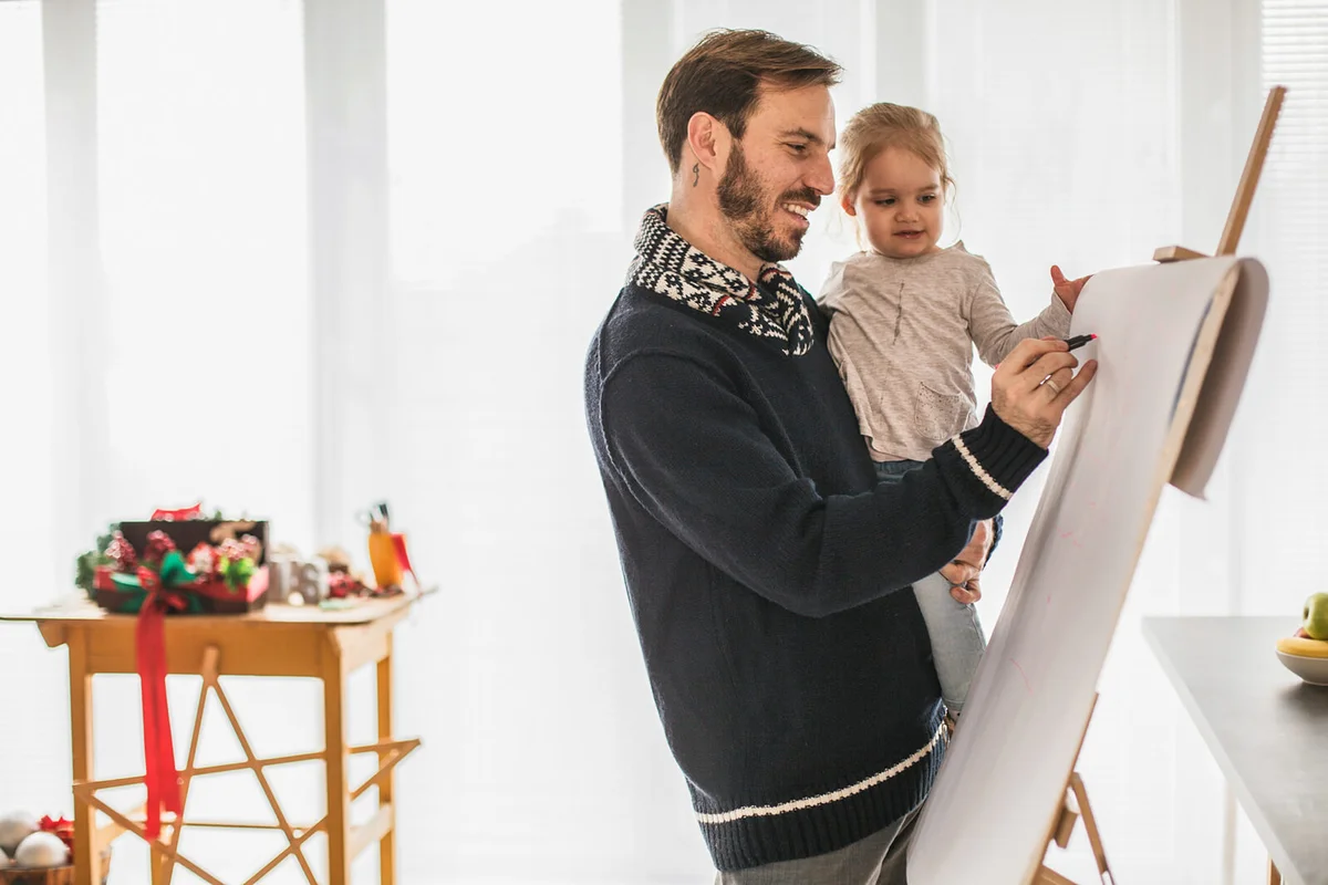 Little girl having fun while drawing on a board with her father