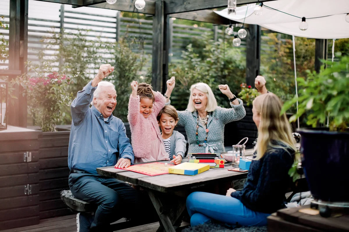 Cheerful family playing board game while sitting at table in backyard