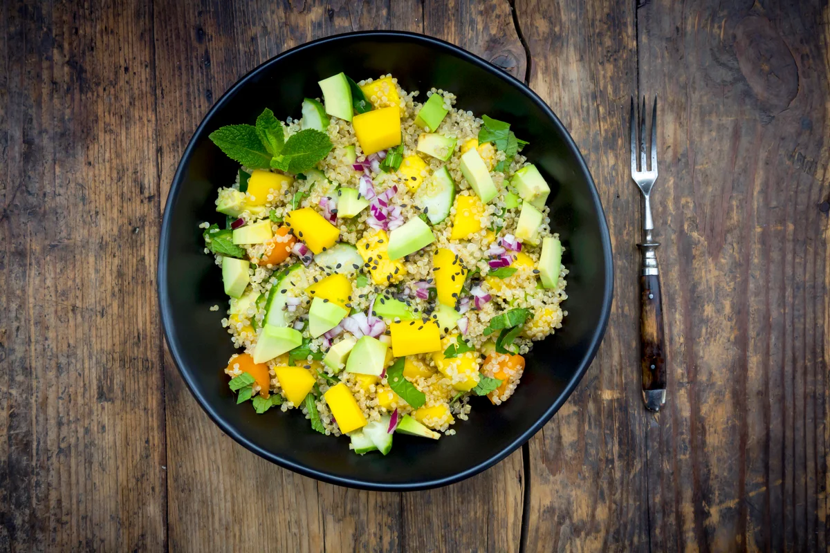 Bowl of quinoa salad with mango, avocado, tomatoes, cucumber, herbs and black sesame