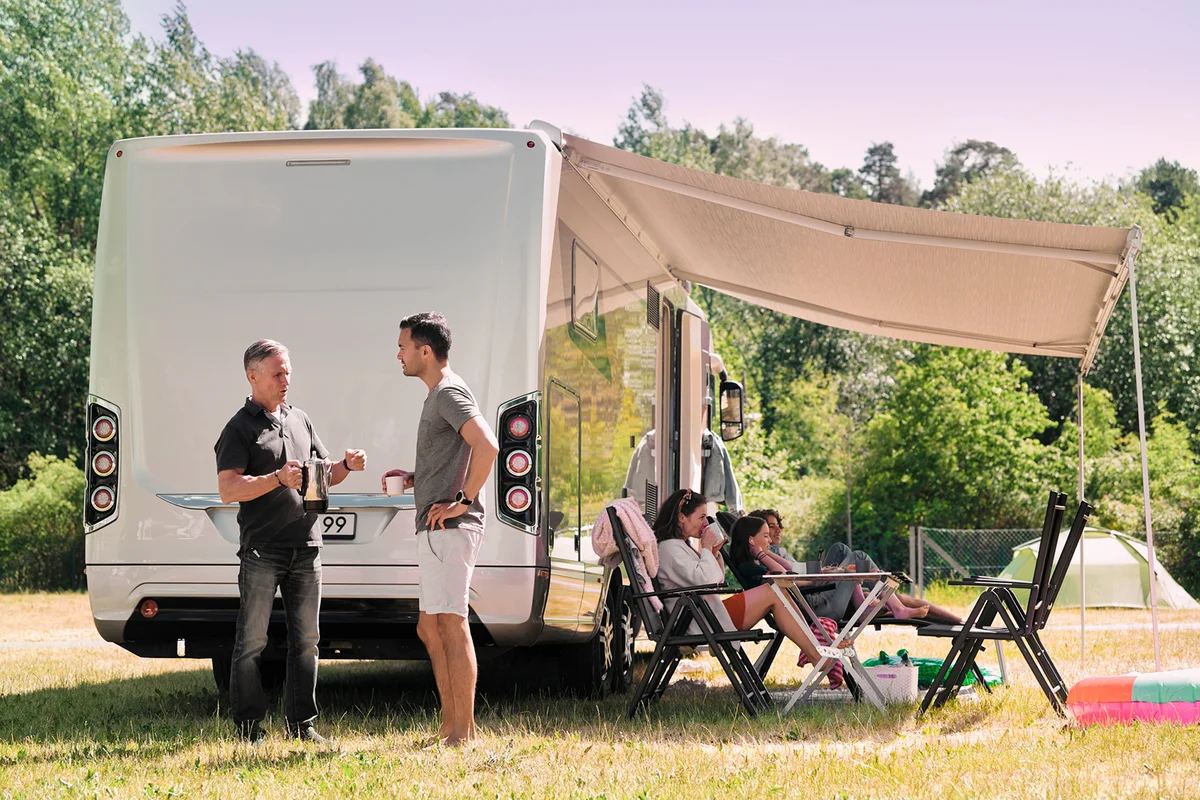 Senior man talking to son while family relaxing outside van at campsite