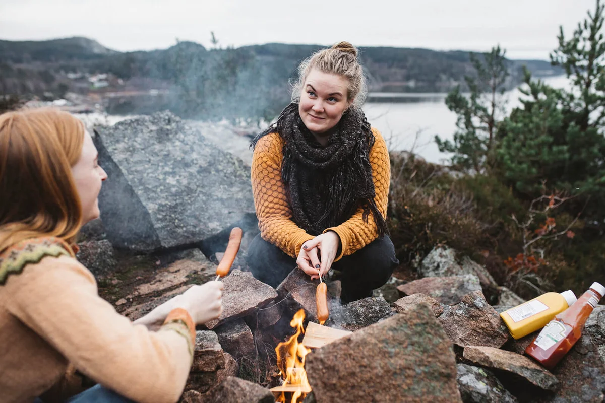 Women preparing hotdogs over campfire