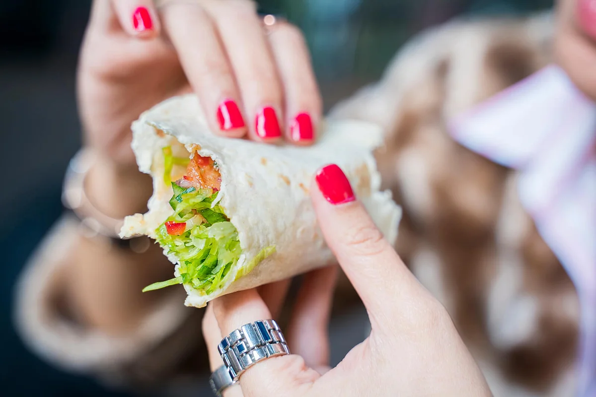 Woman eating a wrap sandwich with han