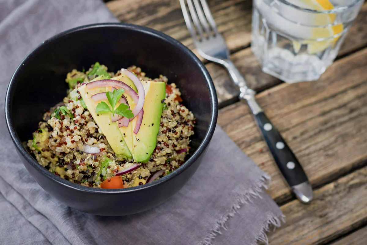 Bowl of Quinoa tricolore with avocado, red onion, tomatoes and flat leaf parsley