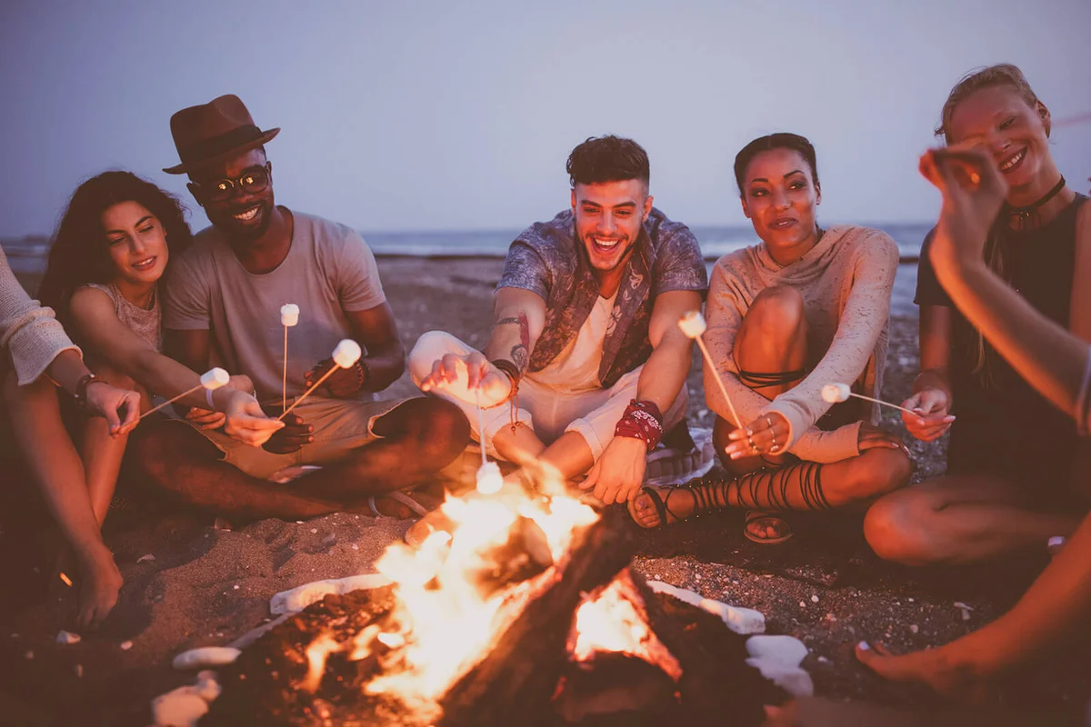 friends roasting marshmallows on sticks at the beach