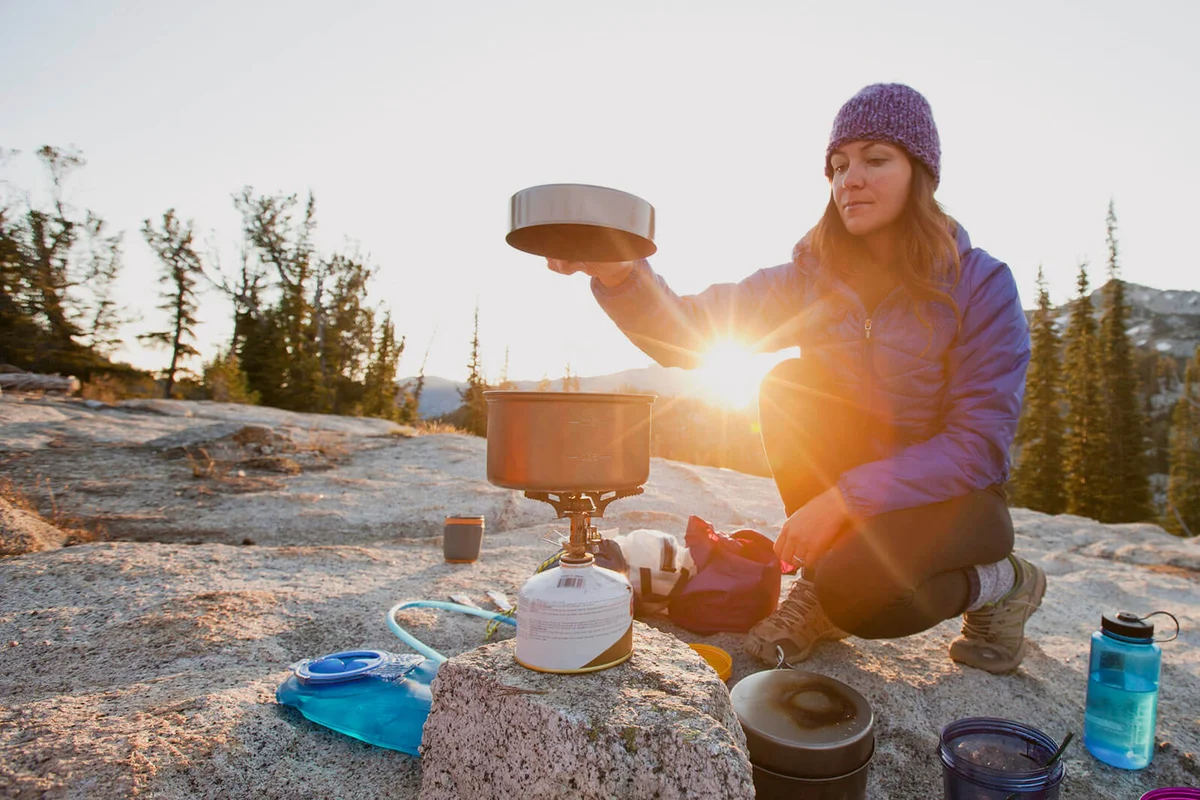 woman cooking breakfast at sunrise while camping in the mountains