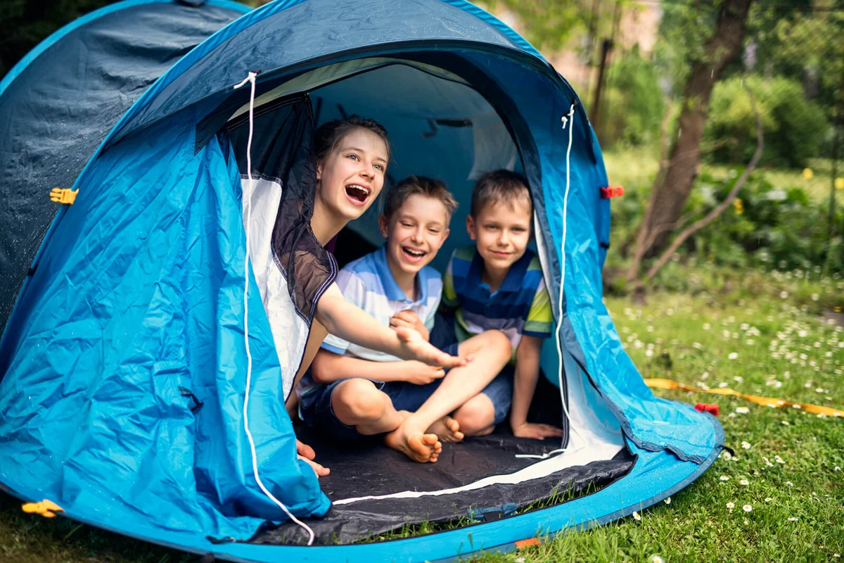 Kids laughing happily sitting inside of blue tent