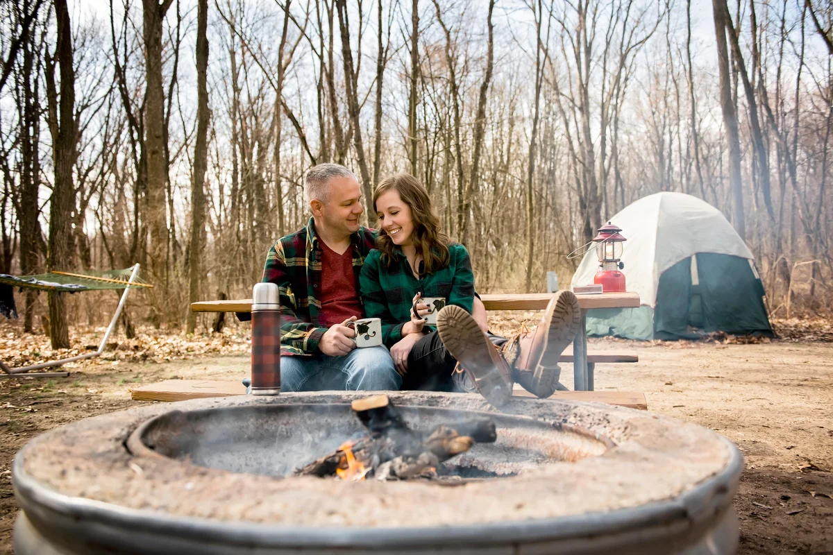 Smiling couple relaxes by campfire drinking coffee