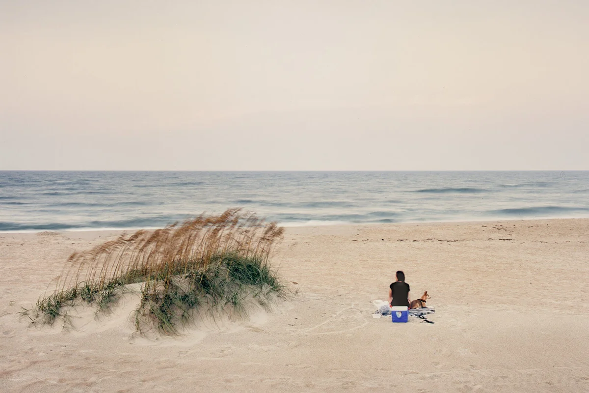Young woman sitting on beach with dog, Ocracoke Island, NC.