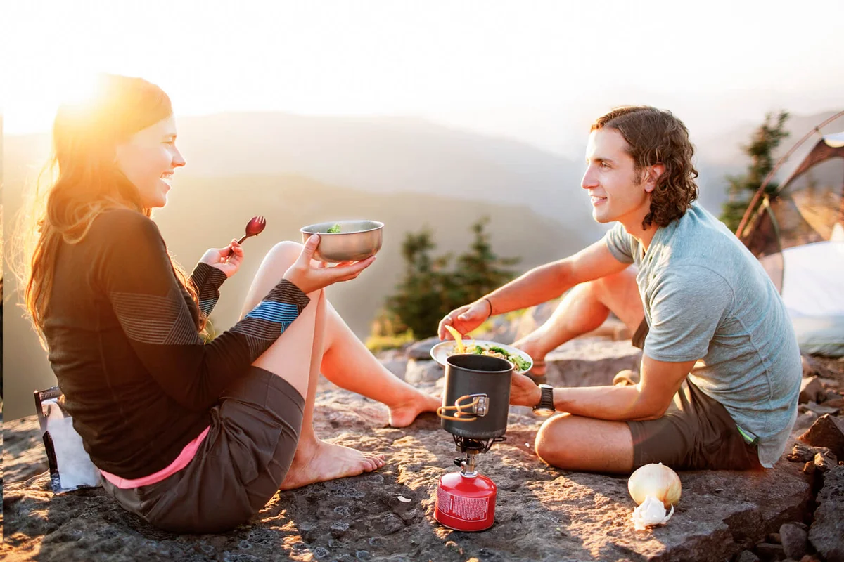 Happy couple having food while sitting on mountain against clear sky