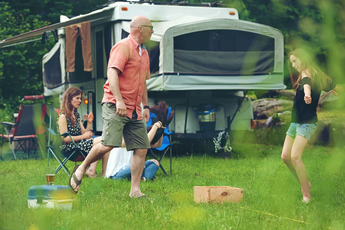 Family playing a game outdoors in front of pop up camper