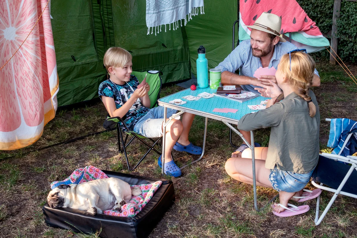 Father with children playing cards front of tent