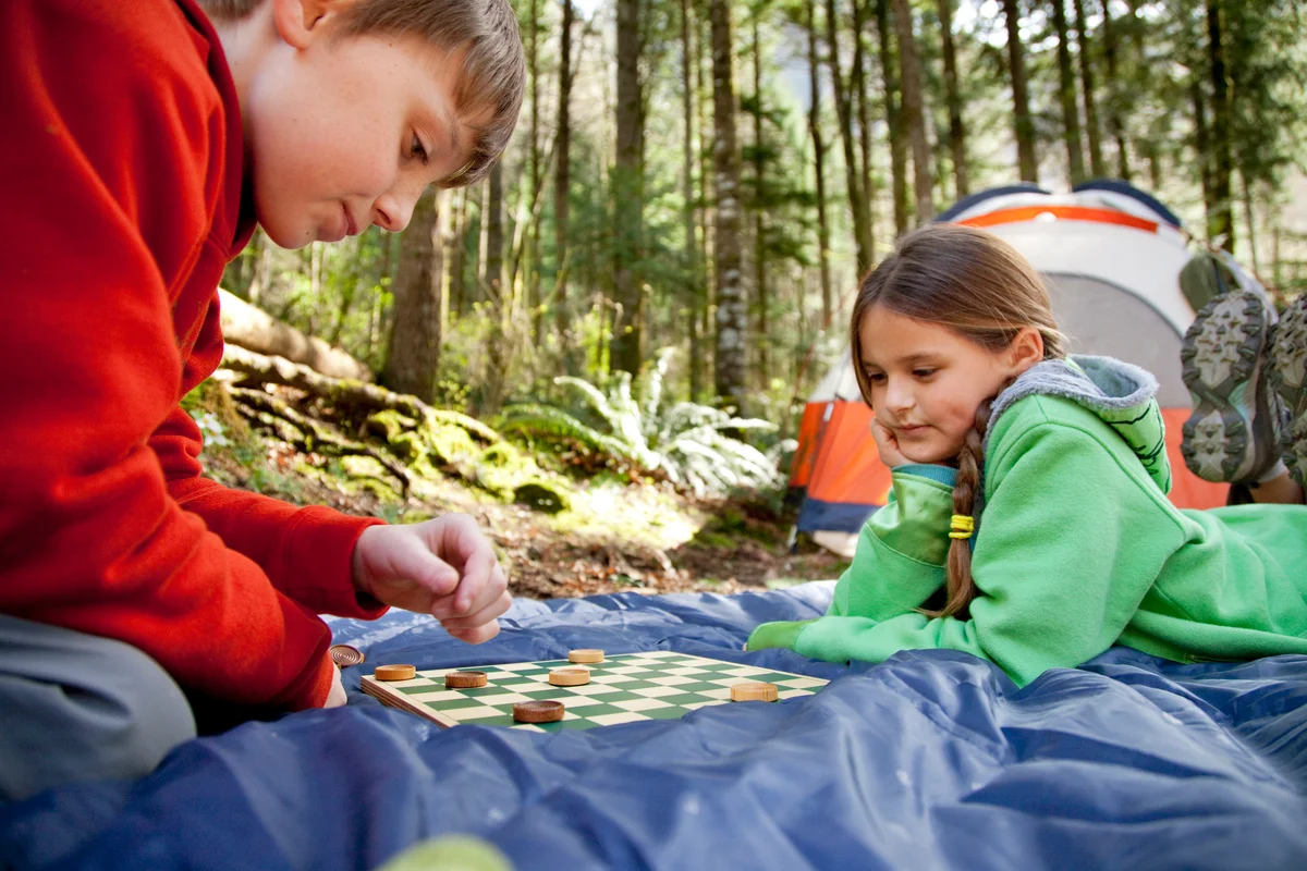 Two young kids play checkers while camping