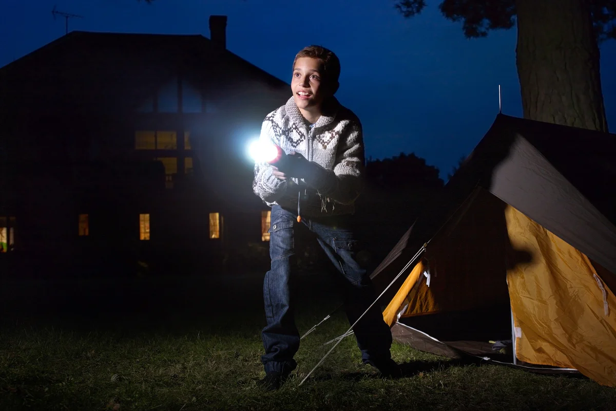 Young boy outside tent shining torch into distance