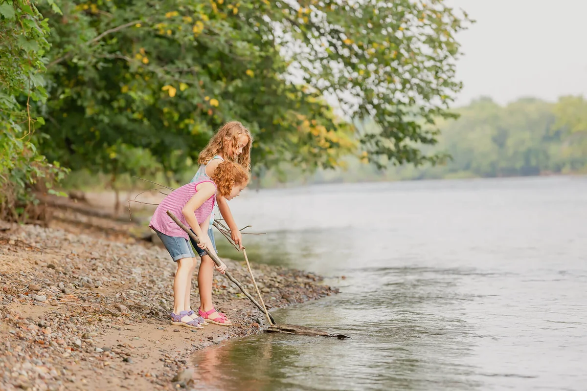 Two young girls (sisters) playing on the bank of the Mississippi River on a summer day in Minnesota