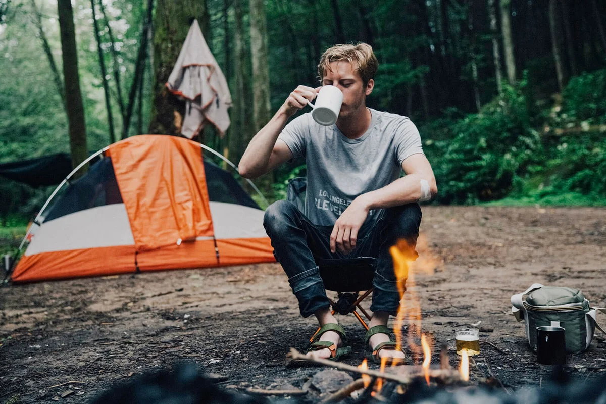 Hiker having drink at campsite in forest
