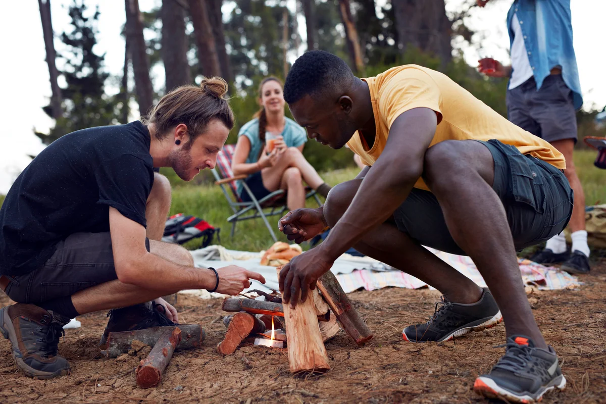 Friends lighting bonfire at campsite