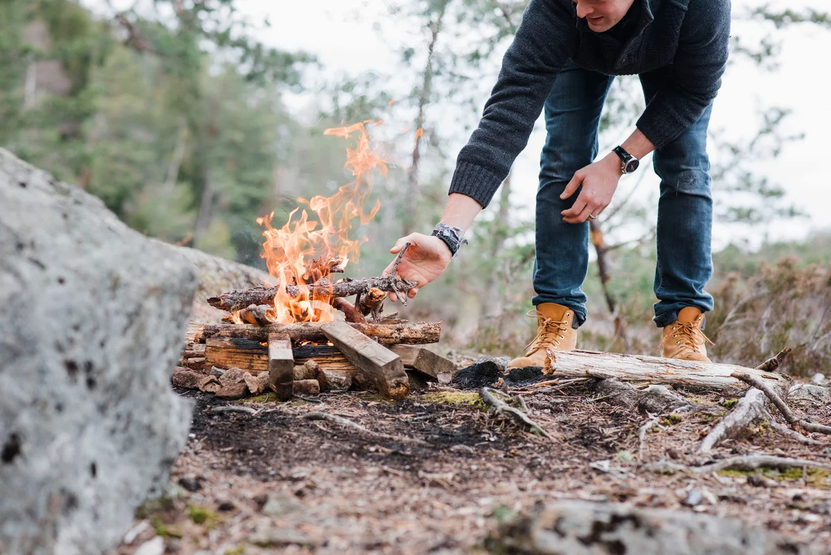 Man putting sticks on a campfire outdoors