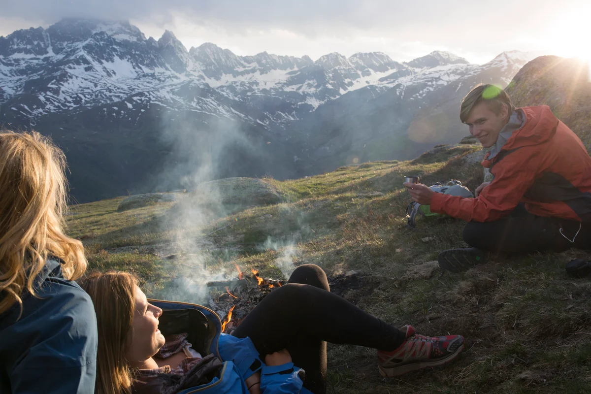 Friends enjoy campfire in mountain meadow
