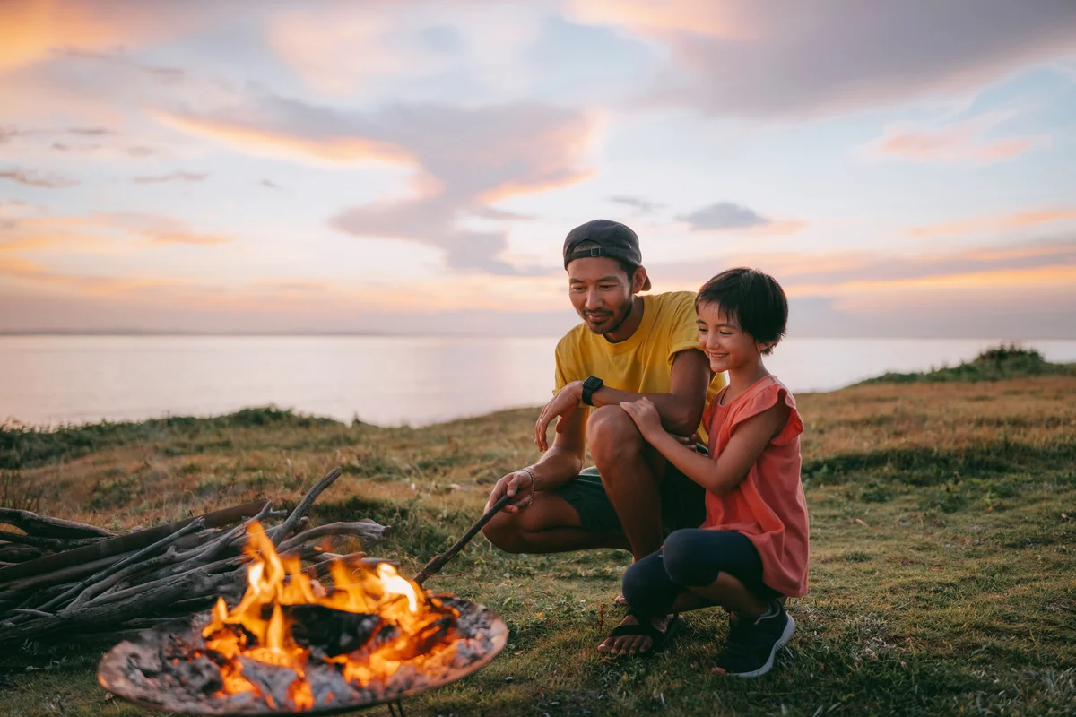 Father and daughter enjoying campfire at campsite at sunset
