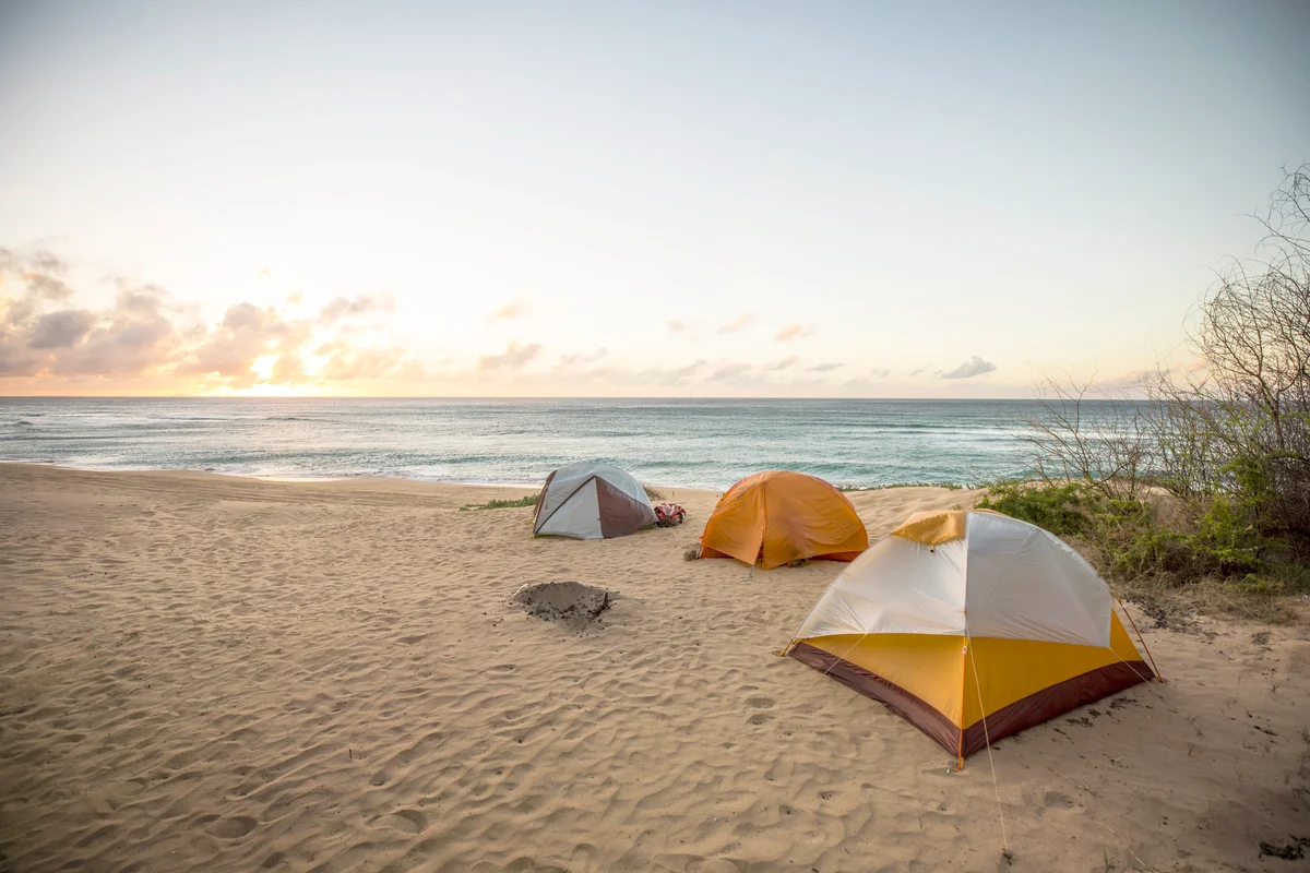 Three tents set up in the sand with the sun setting in the distance