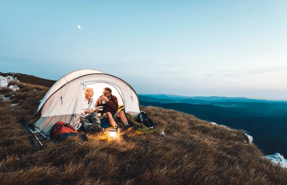 Senior couple camping in the mountains and eating a snack