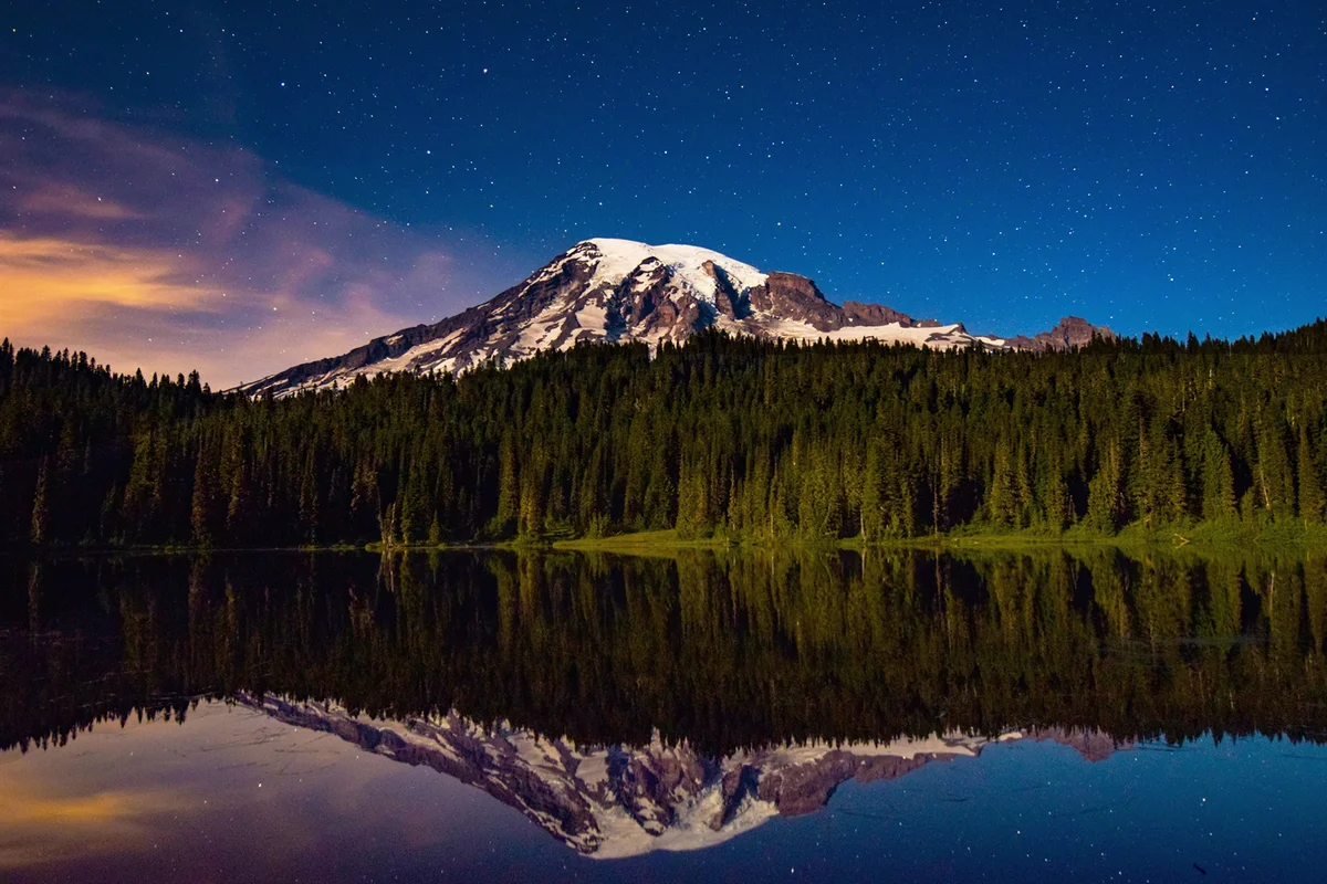 Snowcapped Mountain And Pine Trees Against Sky Reflecting In Lake During Sunrise At Mt Rainier National Park