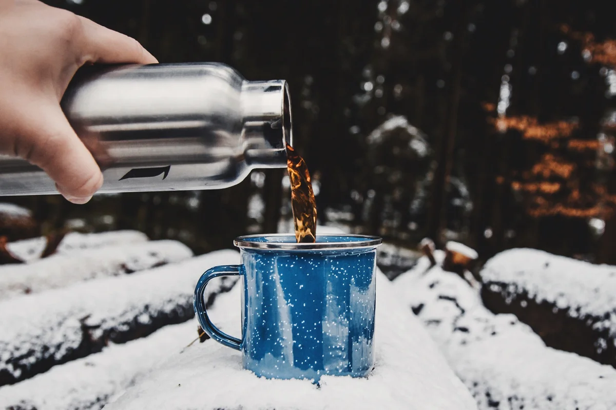 Cropped Hand Pouring Tea In Cup On Snow Covered Log