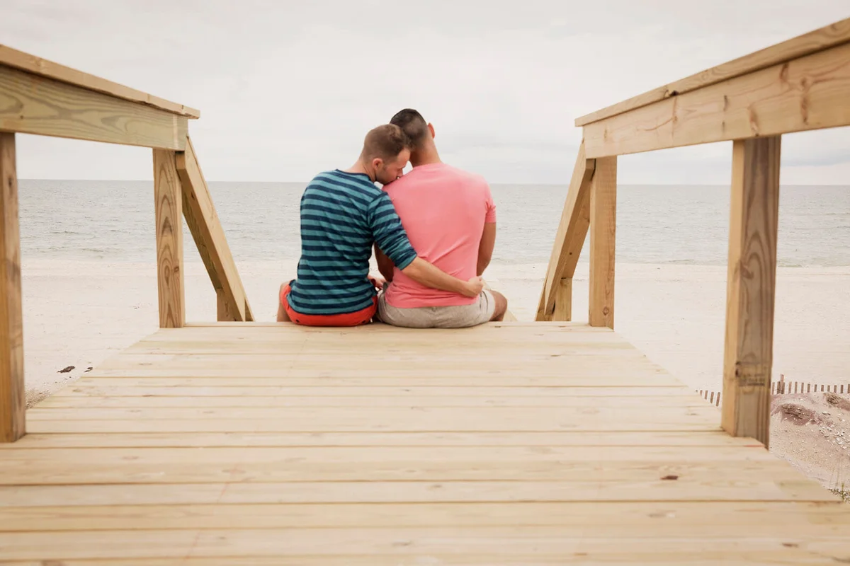 couple sitting on boardwalk against sea