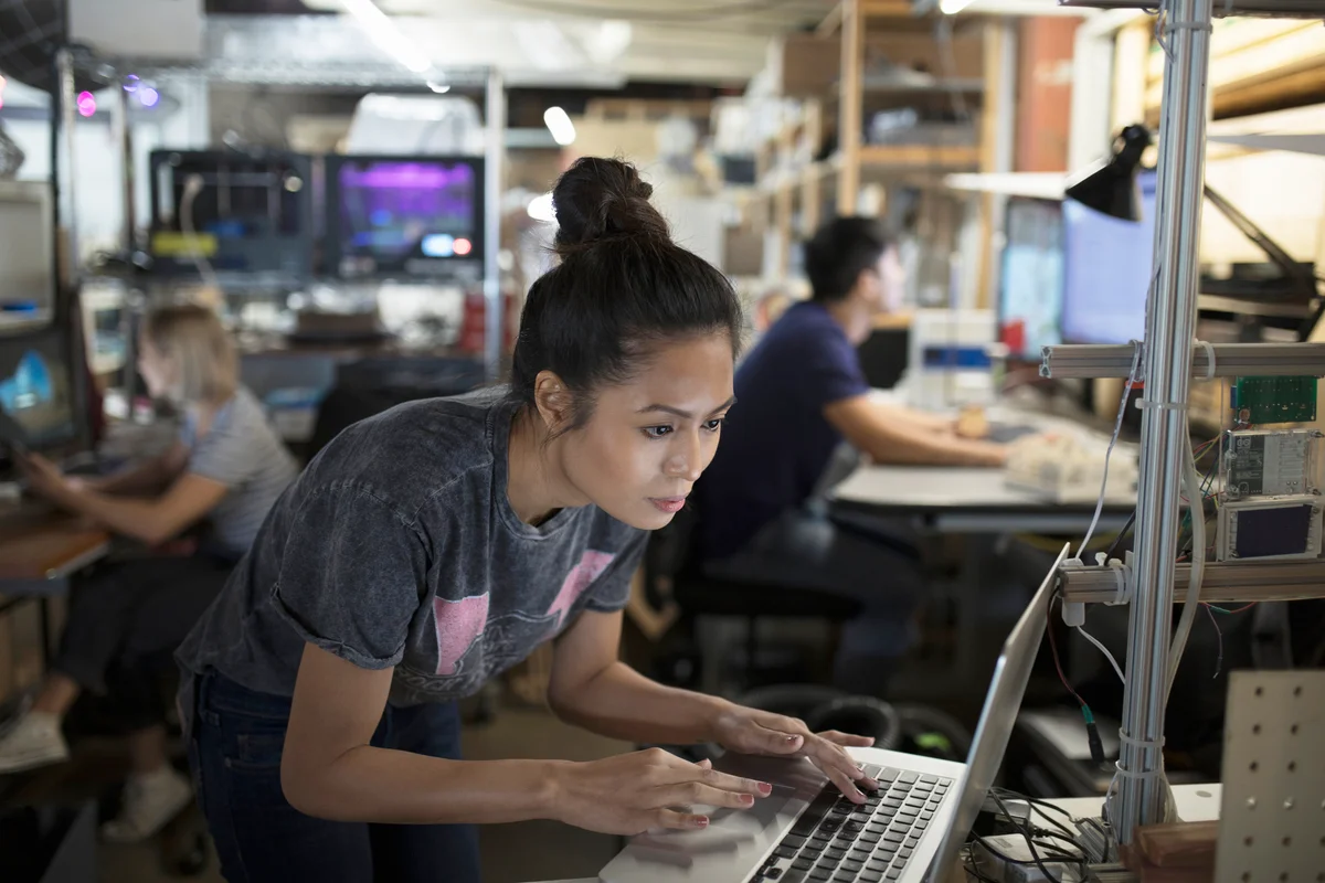 Focused female engineer working at laptop in workshop