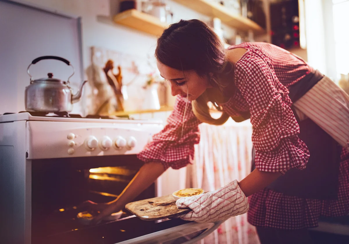 Young woman placing pies in kitchen oven for baking