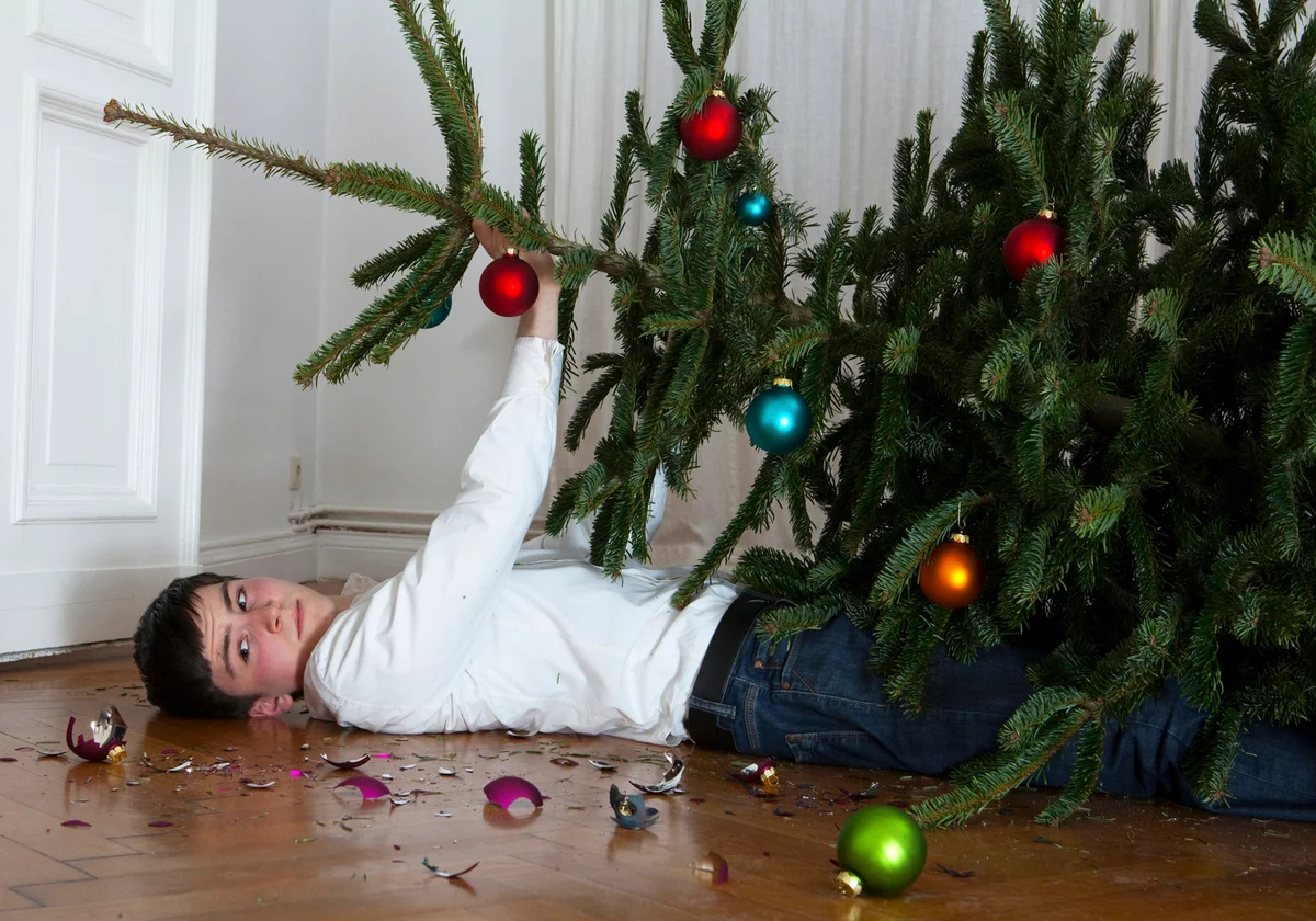 Young man holding up a christmas tree on the floor