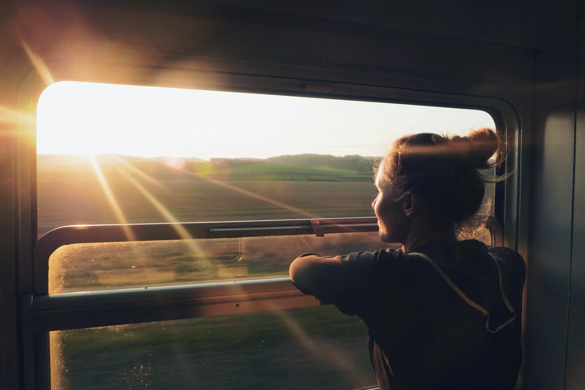 Young Woman Looking Through Window While Traveling In Train During Sunset