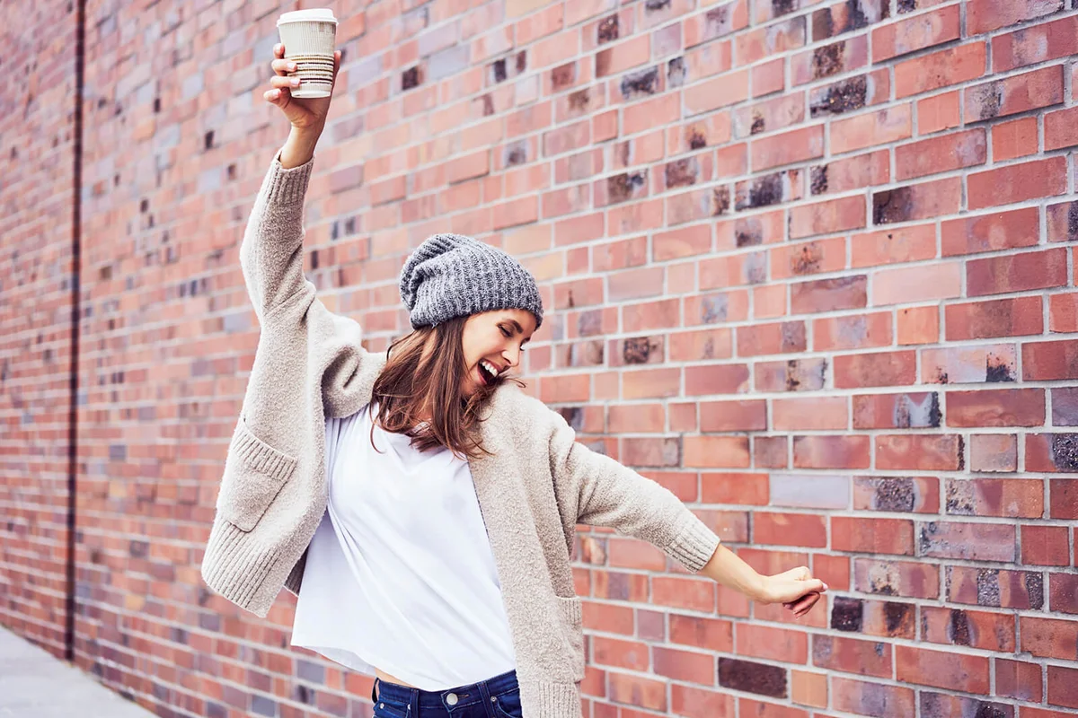 Happy woman with coffee to go singing and dancing on the street