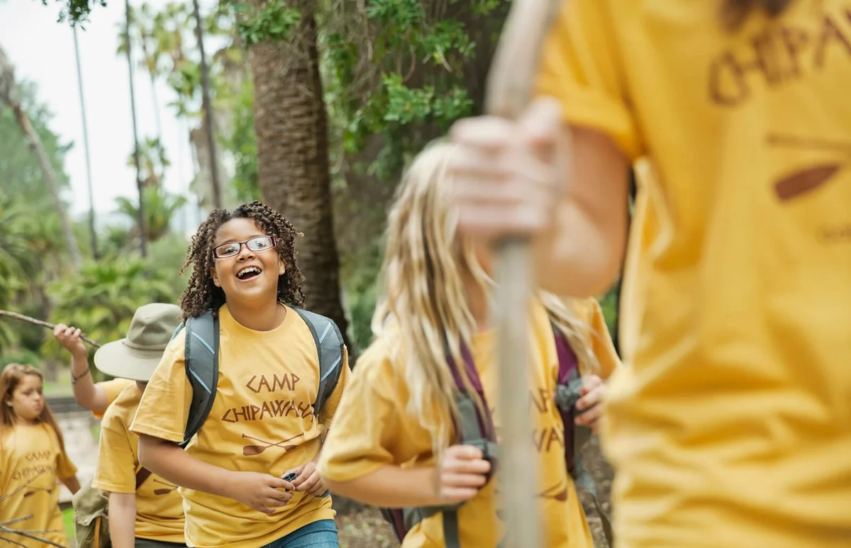 Little girl smiling while walking with friends and camp counsellor in forest